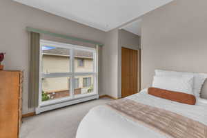 Bedroom with light colored carpet, a baseboard heating unit, and a closet