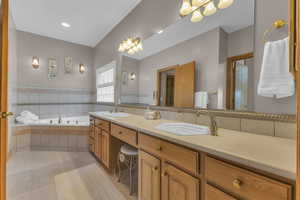 Bathroom with a bath, double vanity, light tile patterned flooring, a chandelier, and tile walls