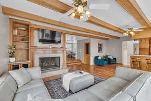 Living room with beam ceiling, wood finished floors, a ceiling fan, a fireplace, and decorative columns
