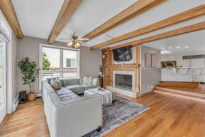 Living area featuring beam ceiling, light wood-style floors, a baseboard heating unit, a premium fireplace, and a ceiling fan