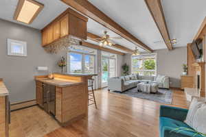 Living area with beam ceiling, a baseboard heating unit, a premium fireplace, light wood-type flooring, and a ceiling fan