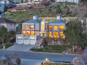 View of front facade featuring a chimney, a balcony, stairs, driveway, and an attached garage