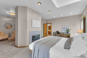 Carpeted bedroom featuring a tiled fireplace, recessed lighting, and a skylight