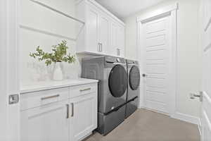 Washroom with additional door to primary suite. Light tile patterned flooring, washing machine and dryer, and cabinet space
