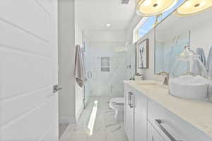 Bathroom featuring vanity, a marble finish shower, light marble finish flooring, and recessed lighting
