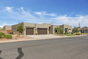 Pueblo revival-style home with stucco siding, an attached garage, and driveway