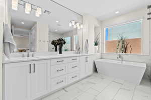 Primary Bathroom featuring light marble finish flooring, double vanity, a freestanding tub, tile walls, and recessed lighting