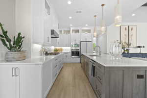 Kitchen with glass insert cabinets, white cabinets, stainless steel appliances, recessed lighting, and a spacious island