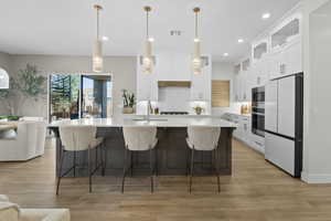 Kitchen featuring white cabinets, hanging light fixtures, a center island with sink, a breakfast bar area, and recessed lighting