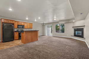 Kitchen featuring dark countertops, black appliances, light carpet, recessed lighting, and open floor plan