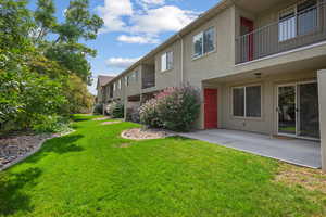 View of grassy yard featuring a balcony and a patio area