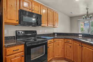Kitchen featuring black appliances, brown cabinets, a chandelier, and dark stone countertops