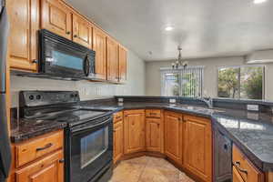 Kitchen with black appliances, brown cabinetry, recessed lighting, a chandelier, and dark stone counters