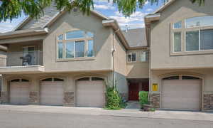 View of front of property featuring stone siding, a garage, stucco siding, and roof with shingles