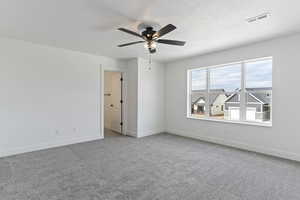 Empty room featuring light colored carpet, ceiling fan, and a textured ceiling