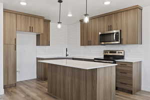 Kitchen with hanging light fixtures, stainless steel appliances, modern cabinets, tasteful backsplash, and brown cabinetry