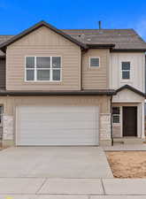 View of front of property with stone siding, board and batten siding, concrete driveway, a garage, and a shingled roof