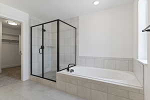 Bathroom featuring a spacious closet, a stall shower, a garden tub, and light tile patterned floors