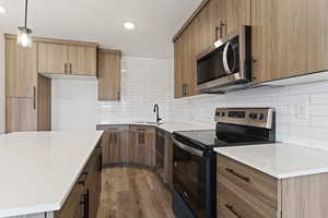 Kitchen featuring appliances with stainless steel finishes, pendant lighting, light wood-style flooring, tasteful backsplash, and light stone counters