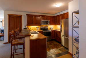 Kitchen with a kitchen breakfast bar, stainless steel appliances, a peninsula, decorative backsplash, and brown cabinetry