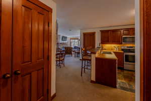 Kitchen with stainless steel appliances, light countertops, a breakfast bar area, and dark colored carpet