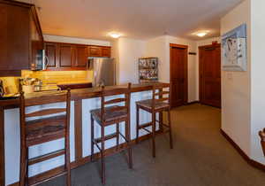 Kitchen featuring a peninsula, appliances with stainless steel finishes, tasteful backsplash, light colored carpet, and a kitchen bar