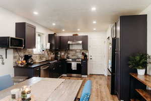 Kitchen with butcher block countertops, stainless steel appliances, laminate  flooring, tasteful backsplash, and under cabinet range hood