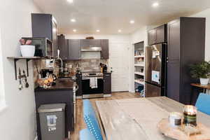 Kitchen with butcher block countertops, stainless steel appliances, backsplash, under cabinet range hood, and laminate floors