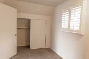 Unfurnished bedroom with light colored carpet, a closet, and lofted ceiling