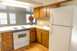Kitchen with white appliances, brown cabinets, light wood-style floors, and tile counters