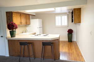 Kitchen featuring brown cabinetry, light wood-type flooring, a peninsula, a breakfast bar area, and white appliances