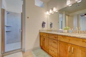 Bathroom with double vanity, a shower stall, a ceiling fan, and light wood finished floors