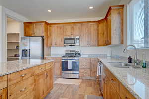 Kitchen featuring appliances with stainless steel finishes, light wood-type flooring, light stone counters, brown cabinetry, and recessed lighting