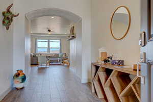 Hall with arched walkways, light wood finished floors, and recessed lighting