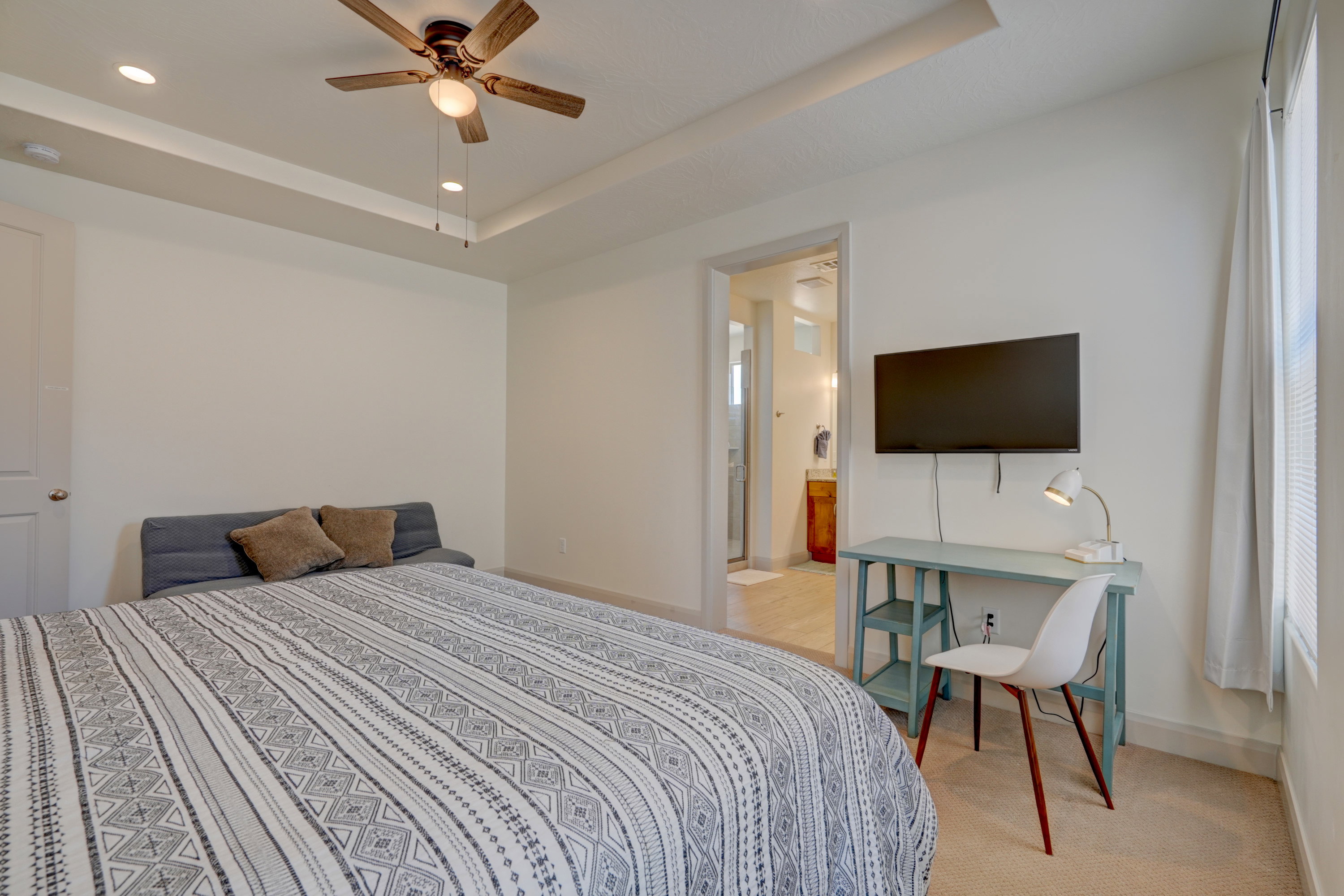 Bedroom with a raised ceiling, ceiling fan, light carpet, recessed lighting, and ensuite bath
