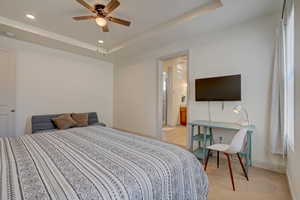Bedroom with a raised ceiling, ceiling fan, light carpet, recessed lighting, and ensuite bath
