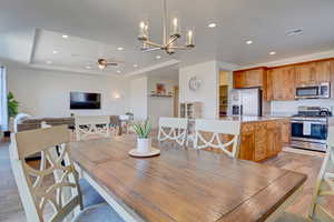Dining area featuring light wood-type flooring, a tray ceiling, a chandelier, recessed lighting, and ceiling fan