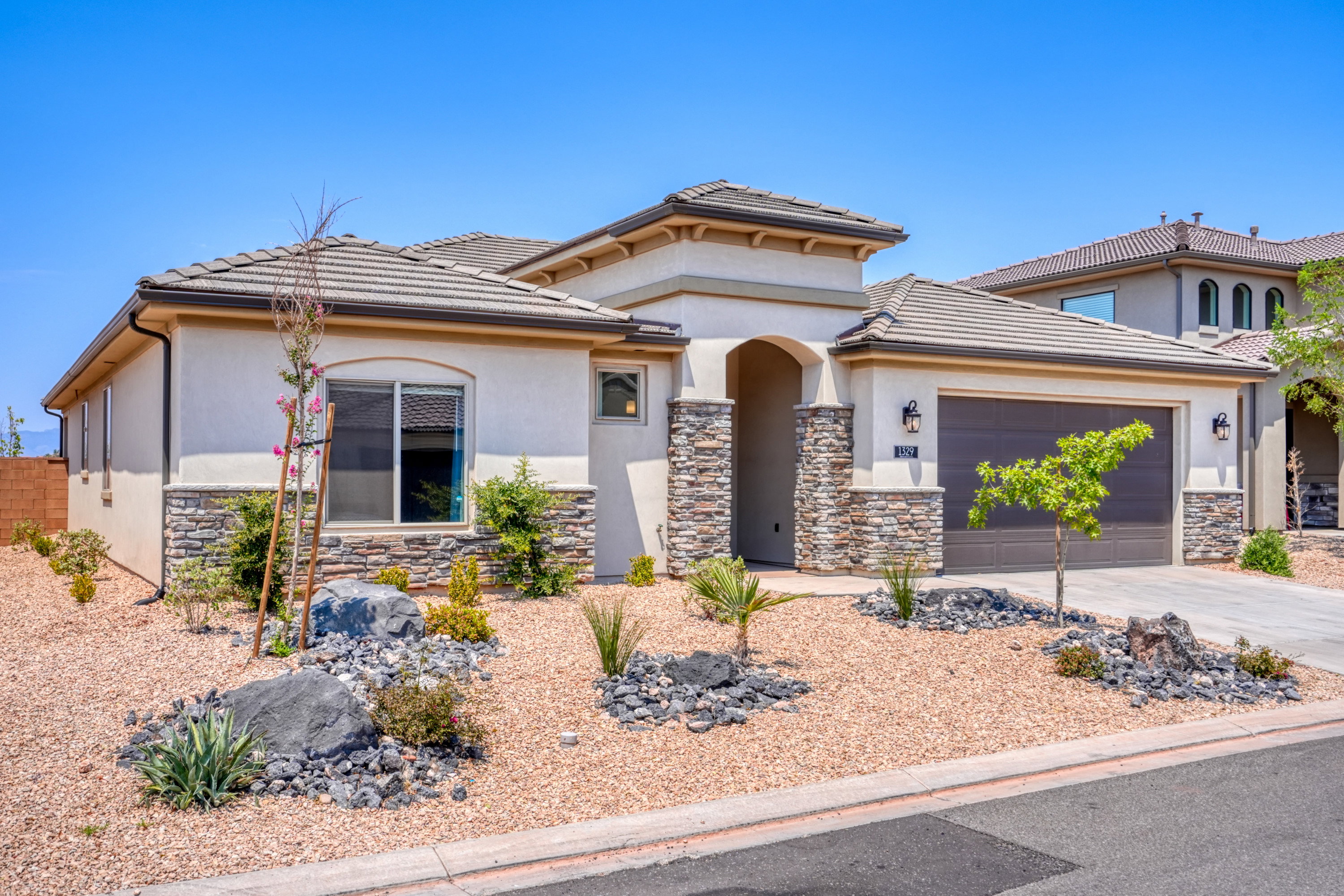 View of front facade with stone siding, driveway, an attached garage, stucco siding, and a tile roof