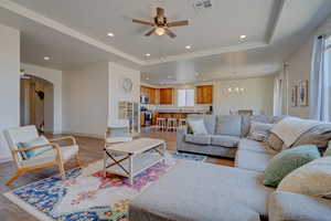 Living room featuring a tray ceiling, recessed lighting, light wood-type flooring, ceiling fan, and a chandelier
