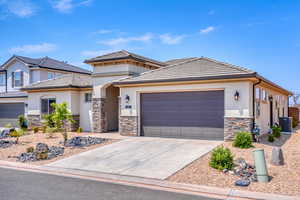 Prairie-style house with stone siding, concrete driveway, stucco siding, an attached garage, and a tile roof