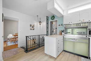 Kitchen with white cabinetry, light wood finished floors, stainless steel oven, light countertops, and a peninsula