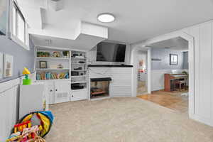 Recreation room featuring light colored carpet, a brick fireplace, a textured ceiling, a wainscoted wall, and light tile patterned floors
