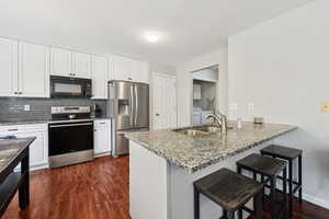 Kitchen with a kitchen bar, stainless steel appliances, light stone countertops, white cabinets, and backsplash