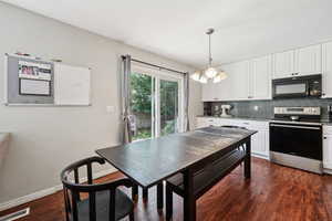 Kitchen featuring stainless steel range with electric stovetop, white cabinetry, decorative backsplash, black microwave, and decorative light fixtures