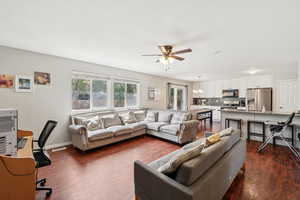 Living area with dark wood finished floors, a ceiling fan, a desk, and a chandelier