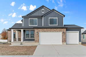 View of front of house with covered porch, driveway, an attached garage, board and batten siding, and brick siding