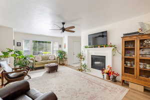 Living area featuring a fireplace with flush hearth, wood finished floors, ceiling fan, and a textured ceiling