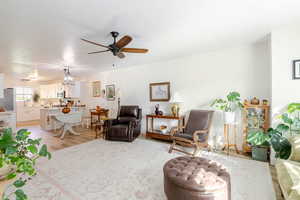 Living area featuring light wood finished floors, ceiling fan, a chandelier, and a textured ceiling