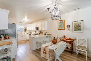 Kitchen featuring light wood finished floors, white cabinets, a peninsula, stainless steel appliances, and a textured ceiling