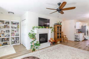 Living area featuring light wood-style floors, a fireplace with flush hearth, ceiling fan, and a textured ceiling